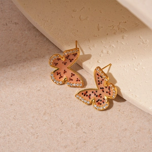 Macro view of gold-plated butterfly earrings with pink enamel dots and zircon crystals