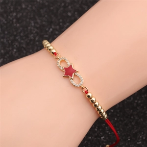 Detailed view of a red cord bracelet featuring a gold infinity symbol and red star charm