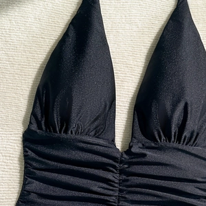 Close-up of black one-piece swimsuit featuring shiny nylon fabric and ruched deep V-neckline