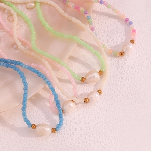 Macro detail of colorful seed beads and freshwater pearls on a wet white surface