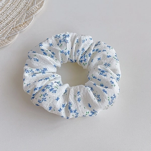 Close-up of a floral scrunchie with blue flowers on white fabric and soft texture