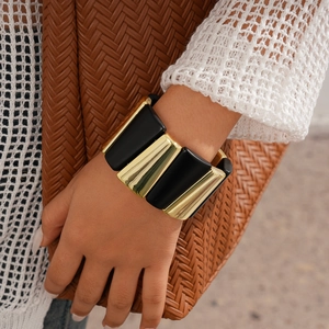 Detail of chunky gold and black geometric acrylic stretch bracelet worn on a wrist