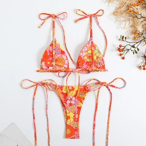 Flat lay of a floral bikini set with vibrant orange patterns and summer beach accessories