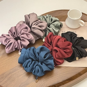 Detailed view of six premium satin hair scrunchies with elegant gold logo charms