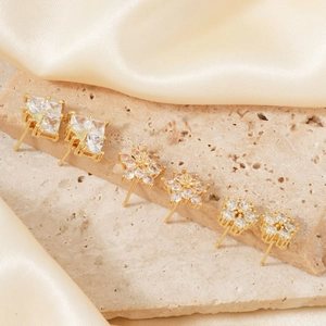Detailed set of geometric zircon stud earrings on stone texture and silk background