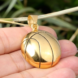 Detail of a shiny gold basketball pendant held in hand for size and texture reference