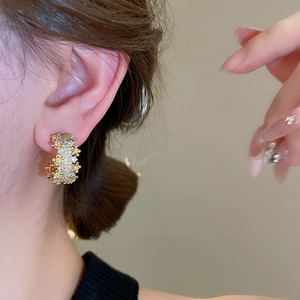 Close-up of gold C-shaped earrings with micro-pave zircons worn by a model