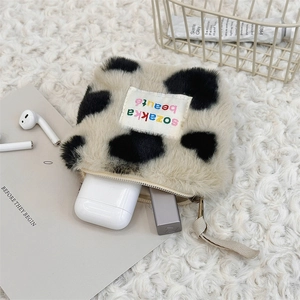 Detailed close-up of a plush cow print mini cosmetic bag with metal zipper on a soft rug