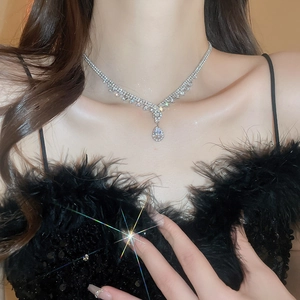 Close-up of a silver V-shaped necklace with a sparkling teardrop pendant on a model
