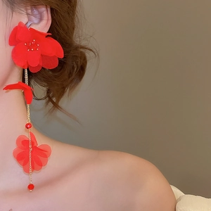 Detail of red fabric flower drop earrings with golden chains on a model's ear