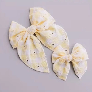 Close-up of yellow and white checkered bow headband with delicate hollow embroidery details