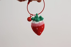 Close-up of handmade crochet strawberry keychain with red bell and steel wire loop