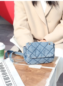 Blue denim quilted chain bag on a wooden table in an outdoor cafe setting