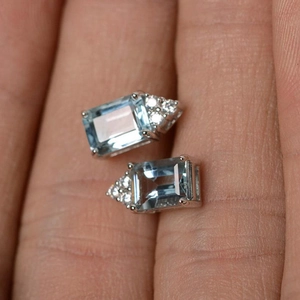 Blue rectangular topaz stud earrings with silver setting and diamond accents on fingers