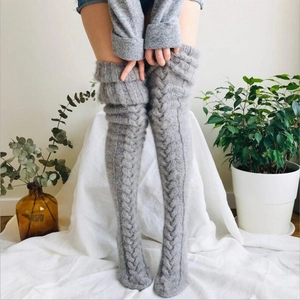 Detail of grey cable-knit over-knee leg warmers showing thick warm texture in home setting