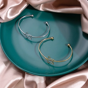 Detailed view of gold and silver cutout star bracelets on a ceramic plate with silk fabric