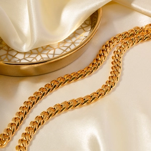 Détail macro d'une chaîne gourmette dorée polie posée sur un tissu en soie blanche