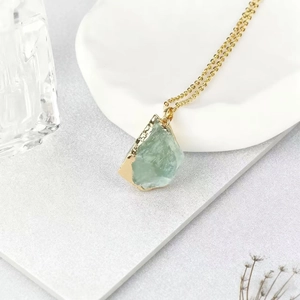 Natural green raw crystal pendant necklace with gold plated edges on a ceramic plate