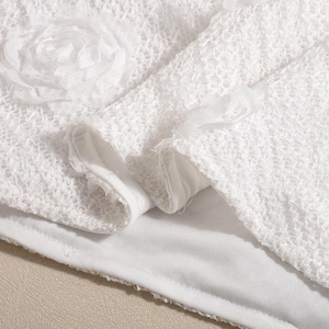 Détail d'une robe en dentelle blanche avec décorations florales 3D et texture en résille