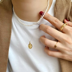 Detail of layered jewelry featuring pearl necklace, coin pendant, and golden rings on model