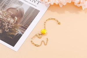 Detail of a gold paperclip link bracelet with yellow geometric bead and heart pendant