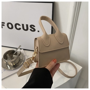 Detail der beigen Mini-Handtasche mit goldfarbenen Beschlägen und Gurt auf weißem Tisch