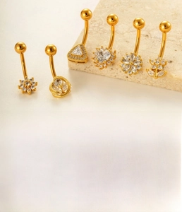 Detail of gold-plated belly rings featuring clover and heart-shaped cubic zirconia charms