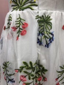 Detaillierte Makroansicht der bunten Blumenstickerei auf dem weißen Netzstoff des Kleides