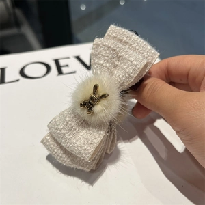 Detailed close-up of a tweed bow hair clip featuring a white fur ball and golden bunny