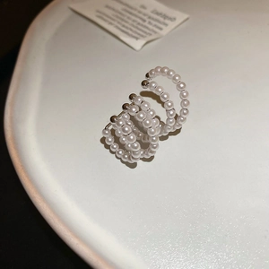 Macro detail of multi-layer pearl ear cuff with silver accents on a white ceramic tray