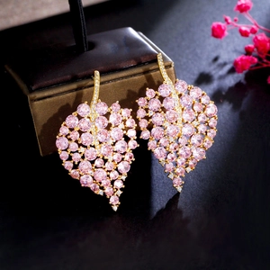 Macro shot of gold-plated leaf earrings with pink cubic zirconia on a jewelry stand