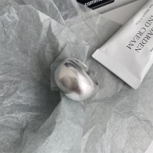 Minimalist wide matte silver ring placed on grey paper with hand cream aesthetic
