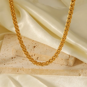 Elegant 18K gold-plated braided chain necklace on a minimalist stone and silk backdrop