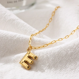Macro shot of 3D bubble letter E necklace in gold finish with textured surface