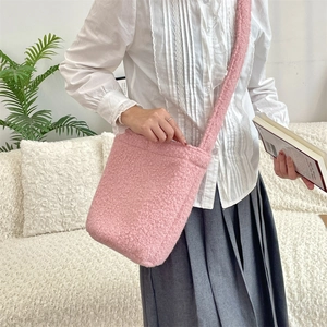 Pink plush faux shearling bucket bag styled as a crossbody in a cozy home setting