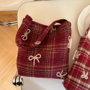 Detail of red plaid wool bag featuring beige crocheted bows and a simple wish label