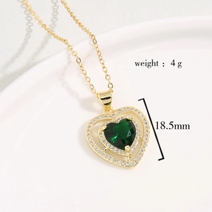 Golden necklace with emerald green heart pendant and zircon stones on a white tray