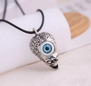 Macro shot of silver skull pendant with blue evil eye detail on a black cord