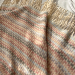 Soft rainbow plaid winter scarf with beige tassels on a white fabric background