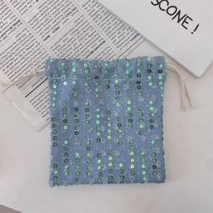 Detail view of light blue denim drawstring bag with green sequins and cotton ropes