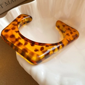 Close-up of retro tortoiseshell resin open bangle resting on a ceramic shell dish