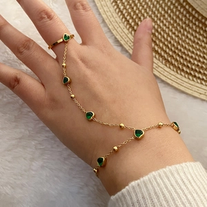 Detail of gold slave bracelet featuring a green heart gemstone on a soft white background