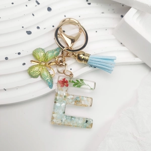 Detailed macro of letter E resin keychain with dried flowers, butterfly and blue tassel
