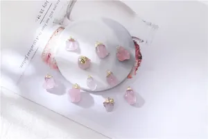 Bulk raw rose quartz pendants with gold caps displayed on white marble stone surface