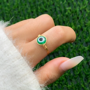 Detail of handmade wire-wrapped gold ring featuring a green evil eye bead charm