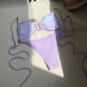 Flat lay of smocked lavender purple bikini with U-shaped metal detail and size S tag