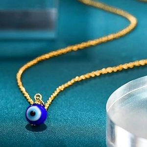Macro shot of a blue Evil Eye charm on a golden twisted rope chain necklace