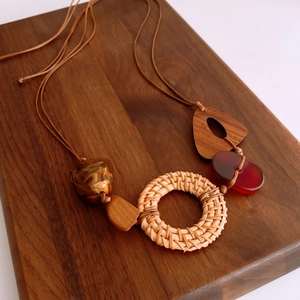 Close-up of ethnic rattan circle and wood triangle pendants on a boho sweater necklace