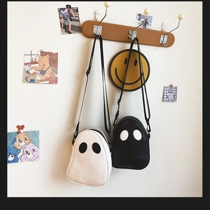 Ghost-shaped PU crossbody bags in black and white hanging on a wooden rack with cute decor