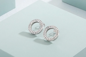 Close-up of silver hollow hoop earrings with inlaid clear rhinestones on a green pedestal